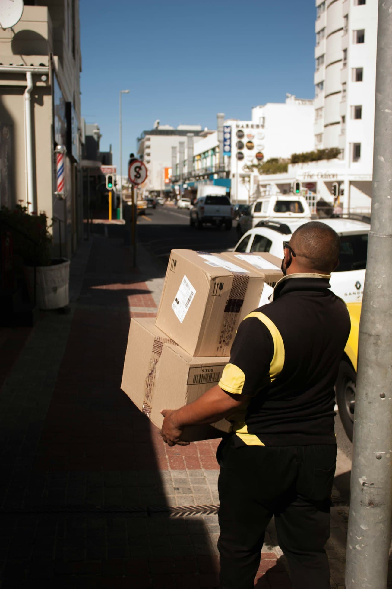 A courier carries two parcels down a sunny street